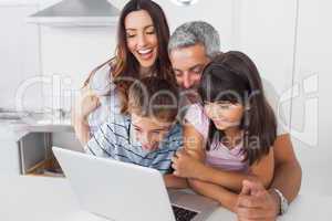 Smiling family sitting in kitchen using their laptop