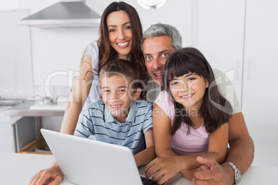 Happy family sitting in kitchen using their laptop