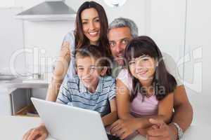 Happy family sitting in kitchen using their laptop