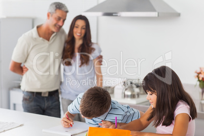 Cute siblings drawing together in kitchen with their parents smi