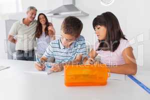 Siblings drawing together in kitchen with their parents smiling
