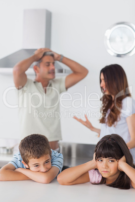 Unhappy siblings sitting in kitchen with their parents who are a