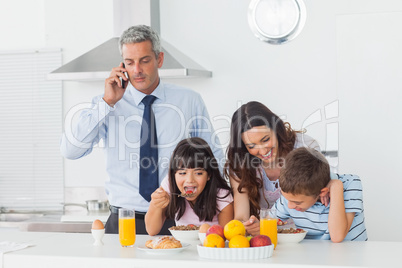Father calling with mobile phone with his family eating breakfas