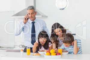 Father calling with mobile phone with his family eating breakfas