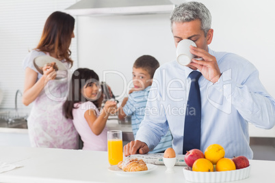 Father drinking coffee while his family are cooking in the kitch