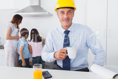 Father wearing hardhat and drinking coffee at home with his fami