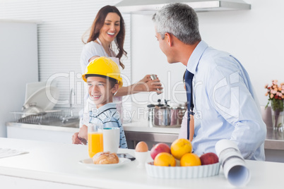 Boy trying on fathers hard hat with parents laughing