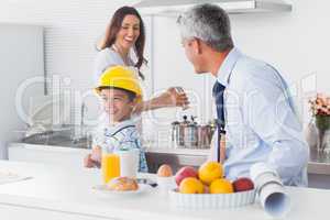 Boy trying on fathers hard hat with parents laughing