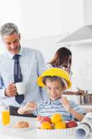Funny little boy wearing hardhat during breakfast with his paren