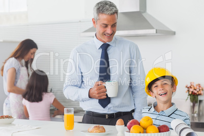 Funny little boy wearing fathers hardhat during breakfast