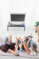 Family sitting on sofa cheering in front of television