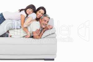 Smiling little girl lying on her parents on sofa
