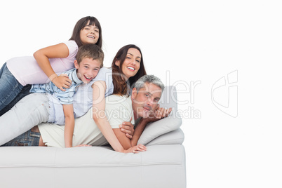 Smiling children lying on their parents on sofa