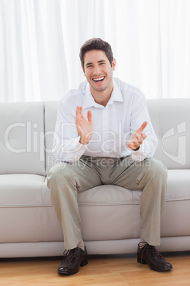 Young man sitting on sofa applauding