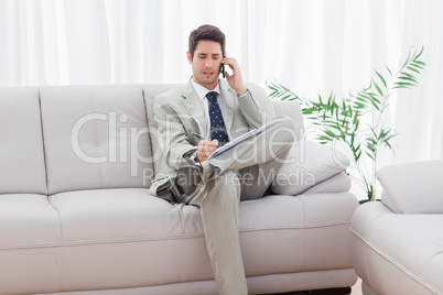 Serious businessman sitting on sofa calling with his mobile phon