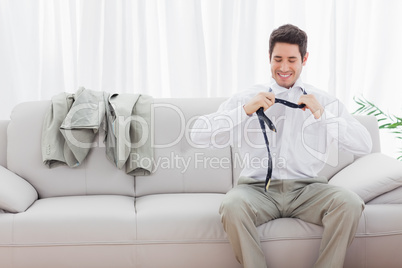 Smiling businessman sitting on sofa loosening his tie