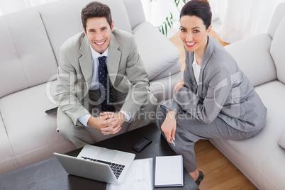 Smiling colleagues working together sitting on sofa and using la