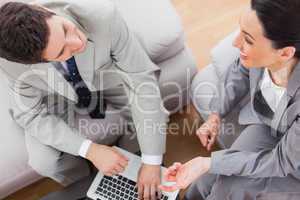 Smiling coworkers talking and using laptop sitting on sofa