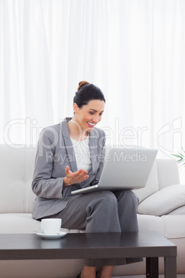 Happy busineswoman sitting on sofa using laptop