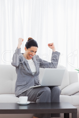 Busineswoman sitting on sofa using laptop cheering