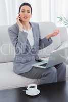 Serious businesswoman calling with her mobile phone and using la