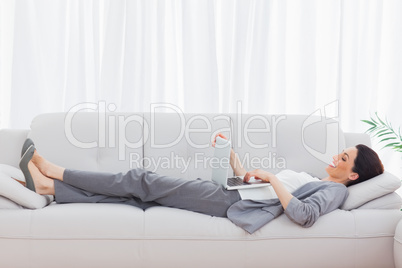 Businesswoman lying on sofa using her laptop