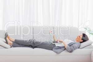 Businesswoman lying on sofa using her laptop