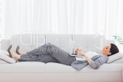 Businesswoman using her laptop lying on sofa