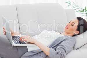 Smiling businesswoman lying on sofa using laptop