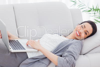 Happy businesswoman lying on sofa using laptop