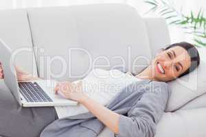 Happy businesswoman lying on sofa using laptop