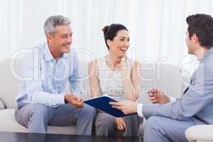 Salesman and clients talking and laughing together on sofa