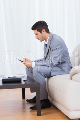 Businessman sitting on sofa texting message with his mobile
