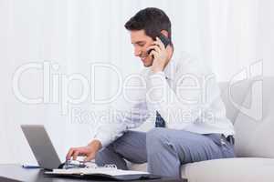 Businessman calling with his mobile phone and using laptop on so