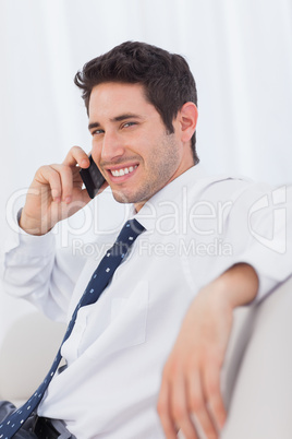 Smiling businessman calling with his mobile phone on sofa