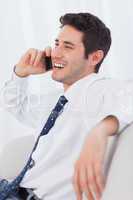 Happy businessman calling with his mobile phone on sofa