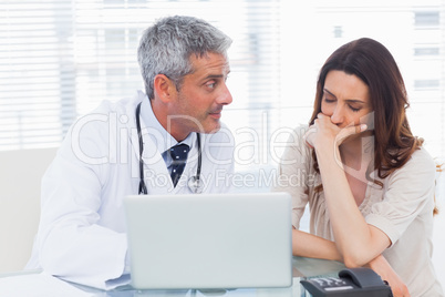 Serious docter showing something on laptop to his patient