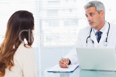 Serious doctor talking with his patient and writing on a noteboo