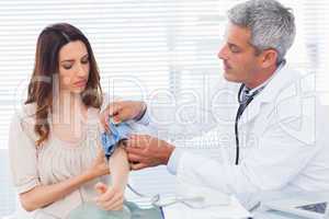 Serious doctor taking blood pressure of his patient