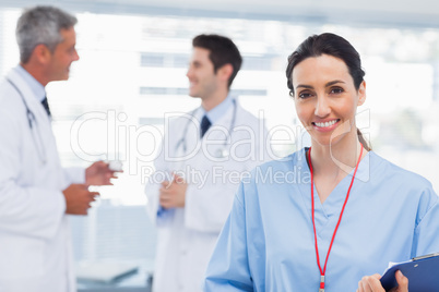 Nurse smiling at camera while doctors are talking together