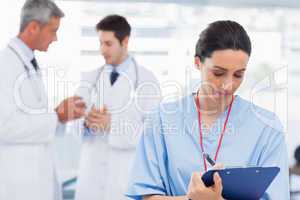 Nurse writing on a clipboard while doctors are talking together