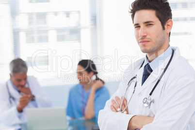 Serious doctor looking at camera with colleagues behind