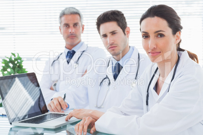 Serious doctors with laptop looking at camera