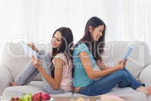 Friends sitting back to back using their tablets