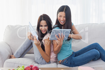 Friends sitting back to back showing each other their tablet pcs