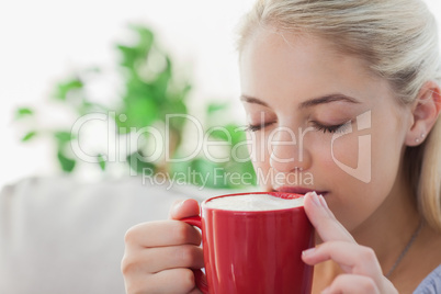 Blonde woman holding a red mug and sipping from it