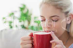 Blonde woman holding a red mug and sipping from it