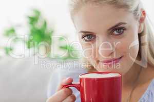 Blonde woman holding a red mug and smiling at camera