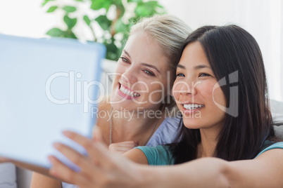 Two pretty friends taking photo with tablet pc