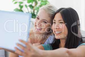Two pretty friends taking photo with tablet pc